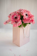 Pink anemone flowers creating a vibrant bouquet, placed inside a elegant pastel gift bag and presented on a clean white surface, conveying themes of gift-giving, appreciation, and celebration