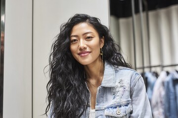 Closeup of a woman smiling in fitting room mirror, adjusting a jacket with subtle pride.