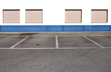 Blue and white plaster wall with four closed brown shutters. Sidewalk and parking in front. Background for copy space