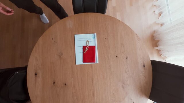 A man enters the room and places a red folder with documents on a wooden table, preparing for a lease or house purchase. Perfect for real estate, rent, mortgage, or property deal visuals.