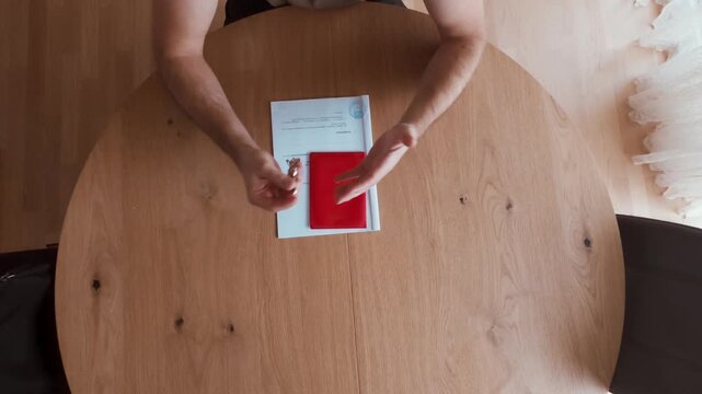 A man sits at a wooden table, explains contract terms, and hands over a red folder containing a rental or purchase agreement. Perfect for real estate, housing, or business negotiation themes.