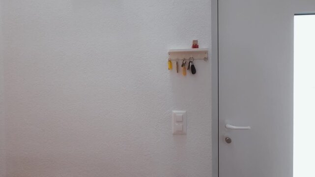 A man hangs his key on a wall-mounted hook next to the entrance door. Simple everyday moment symbolizing home organization, routine, minimalism, and daily life habits.