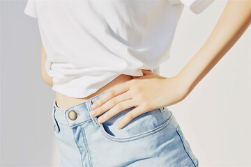 Side view of slim woman in jeans holding waist with hands, symbolizing discomfort or stomach ache. Medical and lifestyle concept with bright background and soft light.