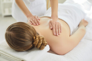 Massage therapist massaging back of woman in spa clinic, holding hands on skin. Female client lying...