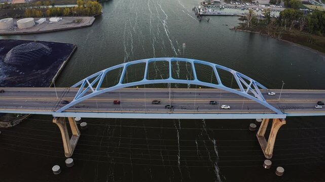 Cars move steadily across the Leo Frigo Memorial Bridge as it stretches over the calm waters of the Fox River, framed by industrial docks and soft evening light.