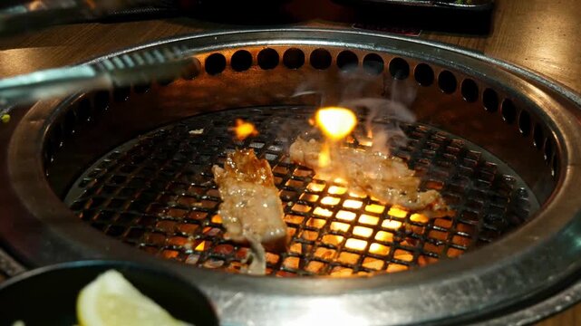 Turning over pieces of beed on yakiniku grill embedded into dining table at a Japanese BBQ restaraunt with tongues
