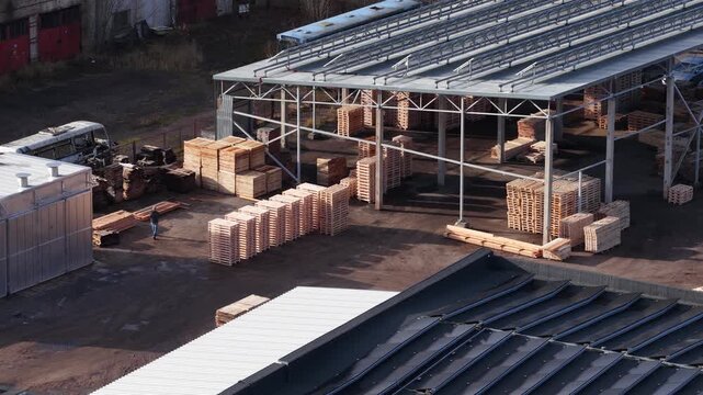 Industrial site with stacked wooden pallets, lumber, and covered storage area, used for wood processing and manufacturing logistics.