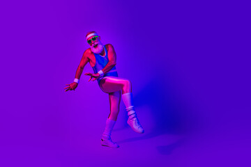 Fototapeta premium Dynamic retro fitness man jumps in neon purple blue studio wearing a jumpsuit and headband for a vibrant lifestyle image