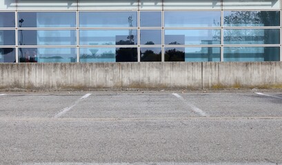 Concrete fence in front of a glass modern building facade with refelctions of an industrial area. Empty parking and street in front. Background for copy space.