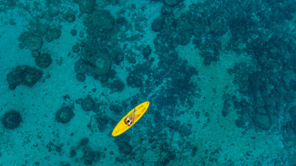 Aerial view woman bright yellow kayak with in the vast expanse of crystal clear turquoise water. The seabeds rocky texture is visible beneath the surface, concept marine environment	