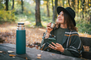 Autumn outdoor relaxation with warm drink, cheerful woman in autumn forest