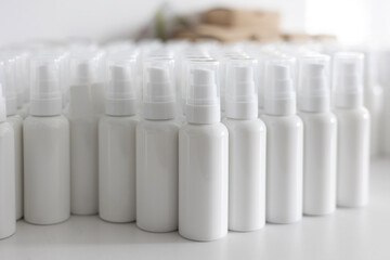 Blank white cosmetic pump bottles, arranged in neat rows on a white surface, are ready for labeling. This packaging is for organic cosmetics, lotion, or serum in a manufacturing lab.