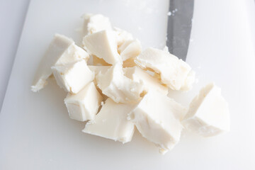 Raw shea butter is cut into chunks on a white cutting board, next to a knife. This is a key ingredient for the craft production of organic cosmetics and natural skincare products in a lab.