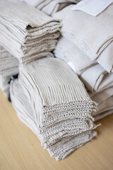 A close-up view of stacked, semi-finished knitwear components in a garment factory. These beige knitted fabric panels, showing the raw texture, are piled on a table, ready for linking and assembly.