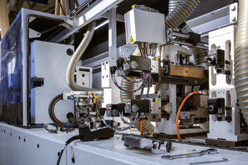 A close-up view of the internal mechanics of an automated edge banding machine. It shows various motors, wiring, and corrugated hoses for dust collection in a furniture factory.