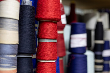 A close-up view of shelves in a knitwear production warehouse. The shelves are filled with many colorful cones of yarn, including red, blue, and black, ready for manufacturing.