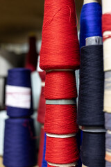 A close-up view of shelves in a knitwear production warehouse. The shelves are filled with many colorful cones of yarn, including red, blue, and black, ready for manufacturing.