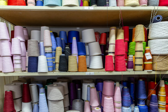 Shelves in a knitwear production warehouse are filled with a large variety of colorful yarn cones. This storage shows the raw materials for knitting, including pink, blue, red, and white threads.
