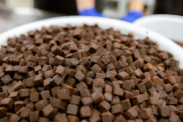 A close-up macro view of small, dark brown brownie cubes. This confectionery, cut into small diced pieces, is a popular ingredient for adding to chocolate, ice cream, or baked goods.