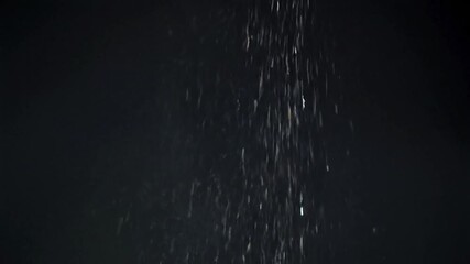 Abstract image of vertical flow, particles glistening against a dark background, suggestive of rain