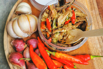 Homemade Sambal Tongkol — traditional Indonesian spicy tuna chili paste with garlic, shallots, and red chili peppers. Authentic Javanese condiment served in a jar on a wooden board. 