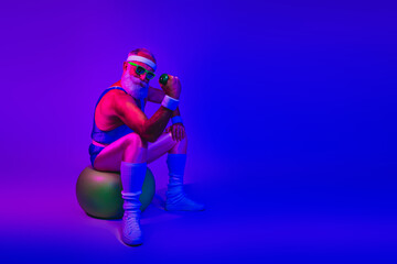 Retro fitness icon sits on a stability ball under neon purple blue lights holding a dumbbell