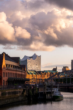 Speicherstadt Hamburg canal and waterfront architecture at sunset with reflection of Elbphilharmonie skyline, showing heritage brick buildings and cityscape design