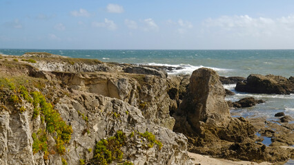 Rugged shoreline featuring weathered cliffs and large rock formations. Waves crash against rocky shore, creating dynamic and wild beauty. Atlantic coastline of Brittany, France.