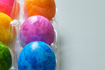 Plastic egg rack with colorful hand-painted Easter eggs in purple, blue, orange and yellow on a gray background. Image with copy space.	