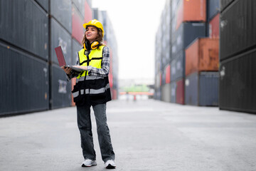 A woman wearing a yellow vest and a hard hat is holding a laptop