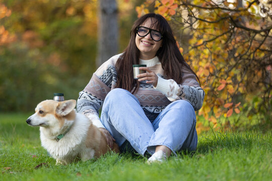 A young woman sits in a park with her pet. A smiling girl enjoys the autumn scenery.