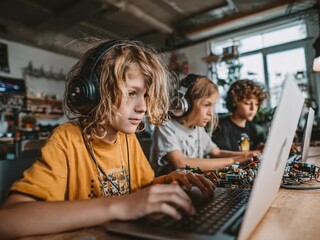 Children Coding and Learning: Young, engaged students immerse themselves in learning through technology, coding and collaborating using laptops and headphones. A modern image of future learning. - Powered by Adobe