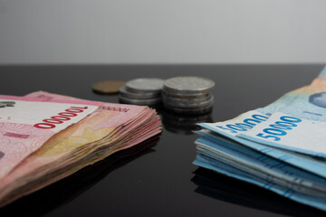 A pile of banknotes and coins on a glossy black table, Indonesian currency