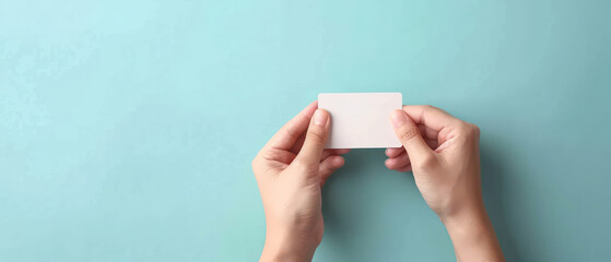 Pair of hands holding blank white card against light blue background, minimalistic and clean