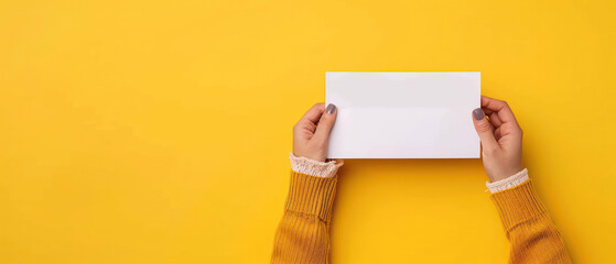 Person holding blank white card with both hands against yellow background casual style cozy