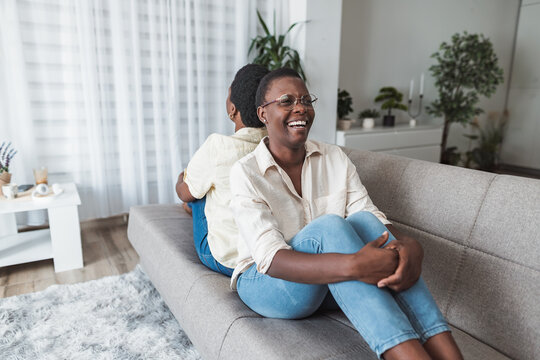Two cheerful african american women relaxing on sofa at home, laughing and enjoying time together