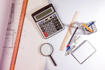 Top view of architect or engineer workplace with blueprints, calculator, ruler, compass, notebook, and magnifying glass. Creative workspace for technical drawing, measurement, and design concept.