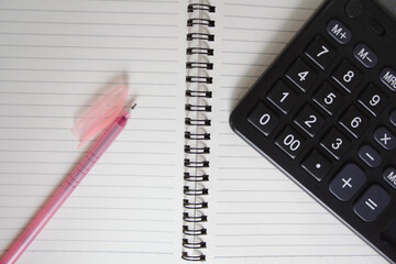 A pink pen and a black calculator sit next to an empty spiral notebook, ready for notes and calculations.