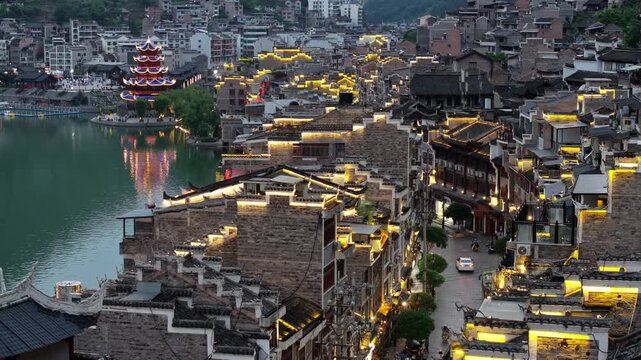 Aerial view of buildings and a pagoda with lights reflecting in the water, creating a mesmerizing scene, Zhenyuan, Guizhou, China.
