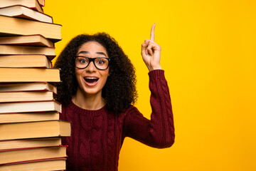 Young mixed race woman with glasses beside tall stack of book bright yellow background celebrating study learning and reading