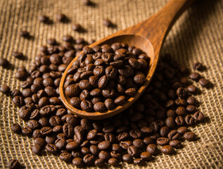 Wooden spoon scooping roasted coffee beans on burlap background