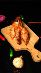 Roasted Chicken on Wooden Cutting Board with Garlic and Chili Peppers in Dark Background