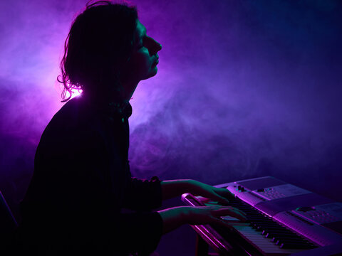 Keyboard player performing on stage with purple haze lighting. Concept of music gear advertising, streaming service branding, and editorial visuals for digital content.