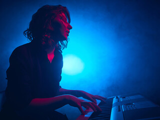 Female keyboardist playing under cinematic blue stage lighting. Concept of music industry...
