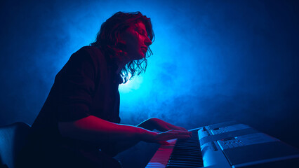 Musician performing at electronic keyboard with bright blue backlight. Concept of music gear and technology advertising, audio product branding, and creative editorial visuals.