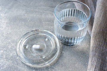 White pill and glass with water stay on the table.