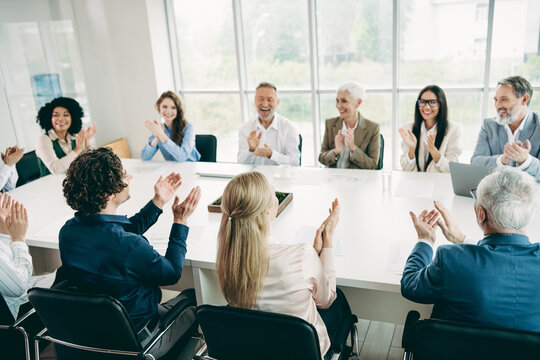 Group of business professionals clapping during a meeting in a modern office setting showing diversity and teamwork