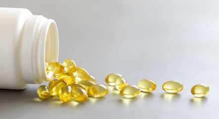 Yellow softgels (gelatin capsules) and bottle on a grey close up. Omega 3 Fish oil or garlic oil