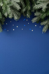 Snowy pine branches with silver and blue star confetti on dark blue background. Merry Christmas...