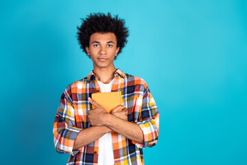 Young multiethnic male student with orange notebook standing with arms crossed against blue background showcasing casual fashion and study